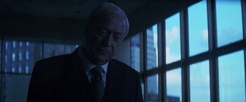 Movie still from “The Dark Knight” (2008), directed by Christopher Nolan – An older man wearing a suit and tie in front of a window; Close Up shot, Over the shoulder angle