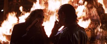Movie still from “The Dark Knight” (2008), directed by Christopher Nolan – A man and a woman talking on a cell phone in front of a fire; Close Up shot, Over the shoulder angle