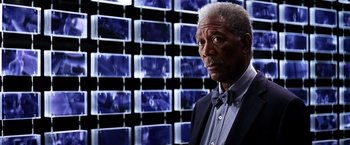 Movie still from “The Dark Knight” (2008), directed by Christopher Nolan – An older man wearing a bow tie in front of a wall of pictures; Close Up shot, Over the shoulder angle