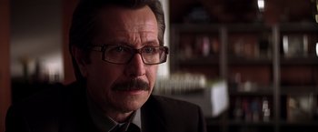 Movie still from “The Dark Knight” (2008), directed by Christopher Nolan – A person wearing glasses and a suit; Close Up shot, Over the shoulder angle