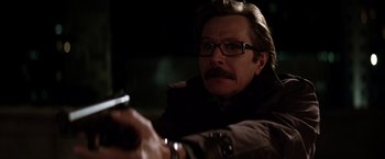 Movie still from “The Dark Knight” (2008), directed by Christopher Nolan – A man with a gun in his hand and glasses; Close Up shot, Over the shoulder angle