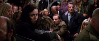 Movie still from “The Dark Knight” (2008), directed by Christopher Nolan – A group of people sitting in a room with people standing around them; Medium shot, Over the shoulder angle