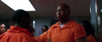 Movie still from “The Dark Knight” (2008), directed by Christopher Nolan – A group of men in orange shirts standing next to each other; Medium shot, Low angle
