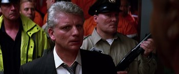 Movie still from “The Dark Knight” (2008), directed by Christopher Nolan – A man in a suit and tie next to another man in an orange shirt; Close Up shot, Low angle