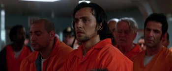 Movie still from “The Dark Knight” (2008), directed by Christopher Nolan – A man in an orange shirt is in a group of people; Close Up shot, Low angle