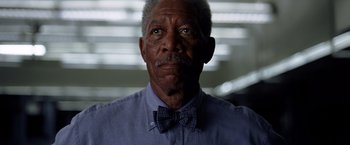 Movie still from “The Dark Knight” (2008), directed by Christopher Nolan – An older man wearing a blue shirt and a bow tie; Close Up shot, Low angle