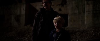 Movie still from “The Dark Knight” (2008), directed by Christopher Nolan – A man standing next to a young boy in a dark room; Medium shot, Over the shoulder angle