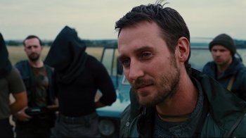 Movie still from “The Dark Knight Rises” (2012), directed by Christopher Nolan – A person with a car in the background; Close Up shot, Over the shoulder angle