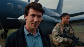 Movie still from “The Dark Knight Rises” (2012), directed by Christopher Nolan – A man standing in front of an airplane with another man standing in the background; Medium shot, Over the shoulder angle