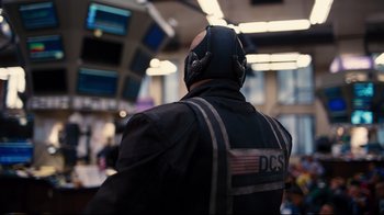 Movie still from “The Dark Knight Rises” (2012), directed by Christopher Nolan – A man wearing a black jacket and headphones; Close Up shot, Over the shoulder angle