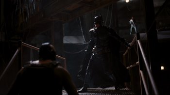 Movie still from “The Dark Knight Rises” (2012), directed by Christopher Nolan – A man dressed as batman standing on some stairs; Wide shot, Over the shoulder angle