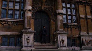 Movie still from “The Dark Knight Rises” (2012), directed by Christopher Nolan – A man standing in front of an entrance to a building; Wide shot, Low angle
