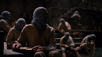 Movie still from “The Dark Knight Rises” (2012), directed by Christopher Nolan – A man with a balaclava sitting in front of a group of people; Medium shot, Low angle