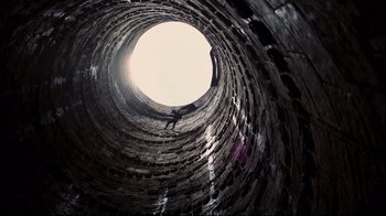 Movie still from “The Dark Knight Rises” (2012), directed by Christopher Nolan – A person sitting inside of an old brick tunnel; Extreme Wide shot, Overhead angle