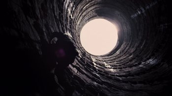 Movie still from “The Dark Knight Rises” (2012), directed by Christopher Nolan – A person standing inside of a tunnel looking up at the sky; Extreme Wide shot, Overhead angle