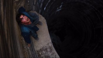 Movie still from “The Dark Knight Rises” (2012), directed by Christopher Nolan – A man is laying on the ground in front of a hole; Wide shot, Overhead angle