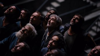 Movie still from “The Dark Knight Rises” (2012), directed by Christopher Nolan – A group of men standing next to each other in a dark room; Wide shot, Overhead angle