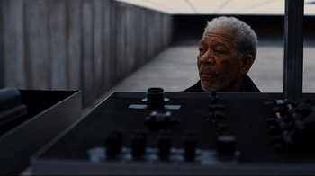 Movie still from “The Dark Knight Rises” (2012), directed by Christopher Nolan – An older man sitting in front of an electronic device; Close Up shot, High angle