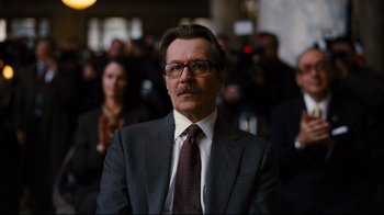 Movie still from “The Dark Knight Rises” (2012), directed by Christopher Nolan – A man in a suit and tie in front of a group of people; Close Up shot, Low angle