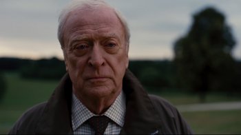 Movie still from “The Dark Knight Rises” (2012), directed by Christopher Nolan – An older man wearing a jacket and a tie; Close Up shot, Low angle