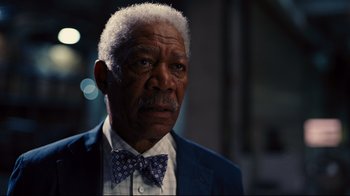 Movie still from “The Dark Knight Rises” (2012), directed by Christopher Nolan – An older man wearing a suit and a bow tie; Close Up shot, Low angle