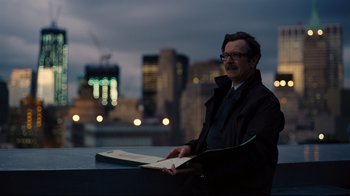 Movie still from “The Dark Knight Rises” (2012), directed by Christopher Nolan – A man in a black jacket holding a book; Medium shot, Over the shoulder angle