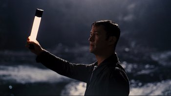 Movie still from “The Dark Knight Rises” (2012), directed by Christopher Nolan – A man holding a cell phone up in the air; Close Up shot, Low angle