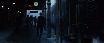 Movie still from “The Girl with the Dragon Tattoo” (2011), directed by David Fincher – A man standing in a train station next to a clock; Wide shot, Low angle