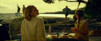 Movie still from “The Girl with the Dragon Tattoo” (2011), directed by David Fincher – A woman sitting on the ground next to a body of water; Medium shot, Over the shoulder angle