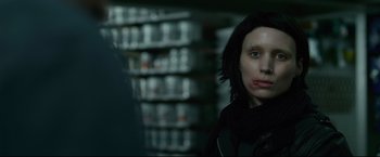 Movie still from “The Girl with the Dragon Tattoo” (2011), directed by David Fincher – A woman with a black jacket on in a dark room; Close Up shot, Over the shoulder angle