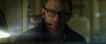 Movie still from “The Girl with the Dragon Tattoo” (2011), directed by David Fincher – A person wearing glasses and holding a pen in his mouth; Close Up shot, Low angle
