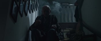 Movie still from “The Girl with the Dragon Tattoo” (2011), directed by David Fincher – An old man sitting on the ground smoking a cigarette; Medium shot, Low angle