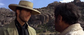 Movie still from “The Good, the Bad and the Ugly” (1966), directed by Sergio Leone – A man wearing a straw hat talking to another man in a field; Close Up shot, Over the shoulder angle
