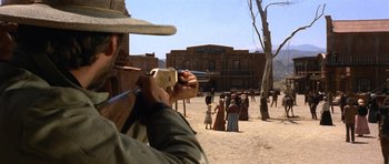 Movie still from “The Good, the Bad and the Ugly” (1966), directed by Sergio Leone – A man holding a gun in front of a group of people; Wide shot, Over the shoulder angle