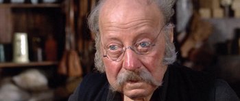 Movie still from “The Good, the Bad and the Ugly” (1966), directed by Sergio Leone – An old man with a beard and mustache wearing glasses; Close Up shot, Over the shoulder angle