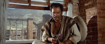 Movie still from “The Good, the Bad and the Ugly” (1966), directed by Sergio Leone – A man holding a gun while sitting in a chair; Medium shot, Low angle