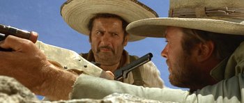 Movie still from “The Good, the Bad and the Ugly” (1966), directed by Sergio Leone – A man in a sombrero holding a gun in front of another man; Close Up shot, Low angle