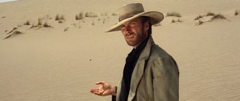 Movie still from “The Good, the Bad and the Ugly” (1966), directed by Sergio Leone – A man in a hat and a jacket standing in the sand; Close Up shot, Low angle