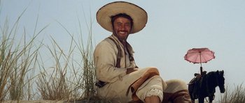 Movie still from “The Good, the Bad and the Ugly” (1966), directed by Sergio Leone – A man sitting on the ground wearing a straw hat; Medium shot, Low angle