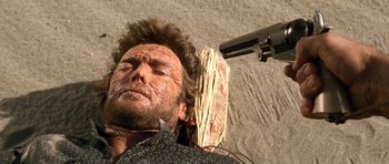 Movie still from “The Good, the Bad and the Ugly” (1966), directed by Sergio Leone – A person laying on the ground holding a gun; Close Up shot, Overhead angle