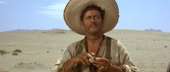 Movie still from “The Good, the Bad and the Ugly” (1966), directed by Sergio Leone – A man wearing a straw hat holding something in his hand; Close Up shot, Low angle