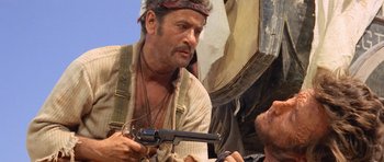 Movie still from “The Good, the Bad and the Ugly” (1966), directed by Sergio Leone – A man holding a gun while standing next to another man; Close Up shot, Over the shoulder angle