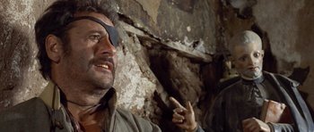 Movie still from “The Good, the Bad and the Ugly” (1966), directed by Sergio Leone – A man with a bandage on his eye points to the side of a wall; Close Up shot, Over the shoulder angle