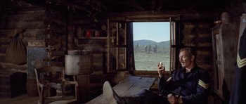 Movie still from “The Good, the Bad and the Ugly” (1966), directed by Sergio Leone – A man sitting in front of an open window with horses in the background; Medium shot, Low angle