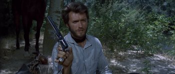 Movie still from “The Good, the Bad and the Ugly” (1966), directed by Sergio Leone – A man holding a gun while standing next to a tree; Close Up shot, Low angle