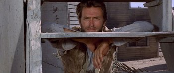 Movie still from “The Good, the Bad and the Ugly” (1966), directed by Sergio Leone – A man with a beard is leaning on a metal railing; Close Up shot, Low angle