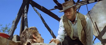 Movie still from “The Good, the Bad and the Ugly” (1966), directed by Sergio Leone – A man in a cowboy hat is shaving another man's beard; Medium shot, Low angle