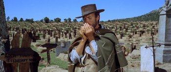 Movie still from “The Good, the Bad and the Ugly” (1966), directed by Sergio Leone – A man with a hat and a blanket around his neck is standing in front of a field of dead trees; Medium shot, Low angle
