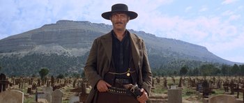 Movie still from “The Good, the Bad and the Ugly” (1966), directed by Sergio Leone – A man with a gun in his hand standing in front of a cemetery; Medium shot, Low angle