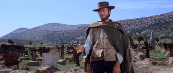 Movie still from “The Good, the Bad and the Ugly” (1966), directed by Sergio Leone – A man holding a gun while standing on top of a hill; Medium shot, Low angle